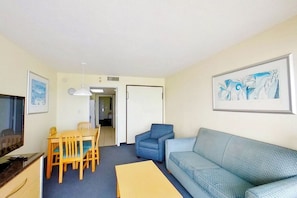 A living room with a sofa, a dining table with chairs, a TV, and artwork on the walls. - Bay Watch Resort 1003 (North Myrtle Beach)