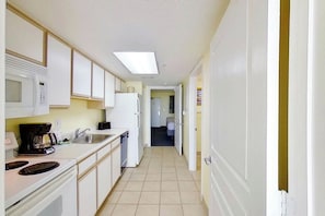 A narrow kitchen with white cabinets, a microwave, a coffee maker, and a refrigerator. - Bay Watch Resort 1003 (North Myrtle Beach)