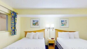 Ein Hotelzimmer mit zwei Betten, einem Nachttisch, einer Lampe und zwei an der Wand befestigten Bildern.