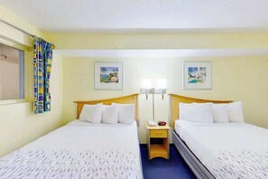 Ein Hotelzimmer mit zwei Betten, einem Nachttisch, einer Lampe und zwei an der Wand befestigten Bildern.