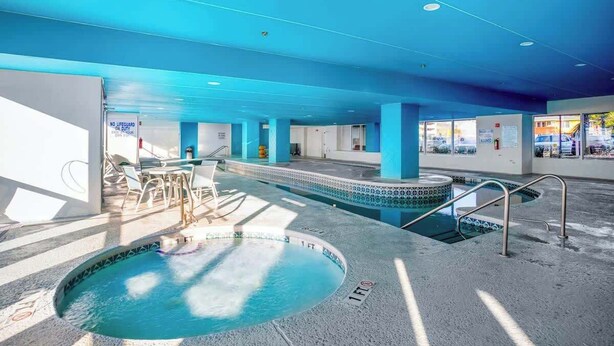 Ein Hallenbad mit blauer Decke, klarem Poolbereich und einer Sitzgelegenheit mit Tischen und Stühlen.