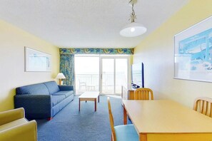 A hotel room with a sofa, a dining table, a TV, and a balcony with a view. - Bay Watch Resort 1006 (North Myrtle Beach)