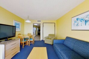 A room with a television, a sofa, a dining table with chairs, and artwork on the walls. - Bay Watch Resort 1006 (North Myrtle Beach)
