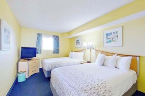 Ein Hotelzimmer mit zwei Betten, einem Fernseher, einem Schreibtisch und einem Mülleimer.