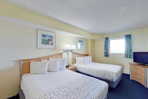 Quarto de hotel com duas camas, televisão, escrivaninha e janela com cortinas.