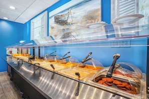 Disposição de buffet com várias estações de serviço, cada uma coberta por uma cúpula transparente e equipada com utensílios.