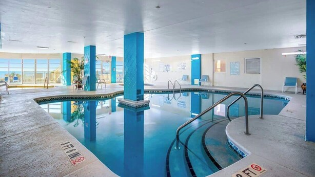 An indoor swimming pool with clear water, blue pillars, and a tiled floor. - Bay Watch Resort 1007 (North Myrtle Beach)