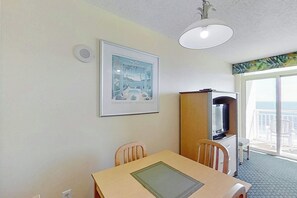 A room with a dining table, chairs, a television, and a large window with a view. - Bay Watch Resort 1007 (North Myrtle Beach)