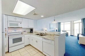 A modern kitchen with a microwave, oven, and dishwasher, a sink, and a dining area with a blue carpet. - Bay Watch Resort 1021 (North Myrtle Beach)
