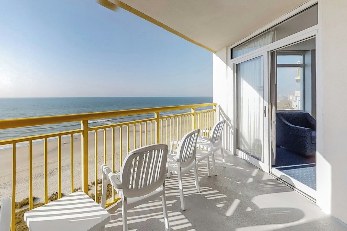 Un balcon avec vue sur l’océan, des chaises blanches et un canapé bleu.