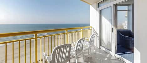 A balcony with a view of the ocean, white chairs, and a blue sofa.