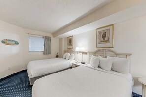 Ein Hotelzimmer mit zwei Betten, einem Nachttisch mit Lampe, einem kleinen Tisch und einem Fenster mit Jalousien.