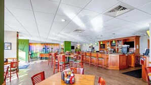 Um restaurante com várias mesas e cadeiras, um espaço de bar e um balcão com uma televisão.