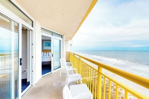 A balcony with a view of the ocean, a bed with white bedding, and a yellow railing. - Bay Watch Resort 1209 (North Myrtle Beach)