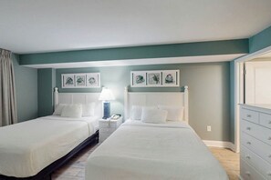 A hotel room with two beds, a nightstand, a lamp, and artwork on the walls. - Bay Watch Resort 1217 (North Myrtle Beach)
