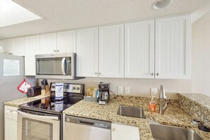 A compact kitchen with white cabinets, a microwave, a coffee maker, and a dishwasher. - Bay Watch Resort 1020 (North Myrtle Beach)