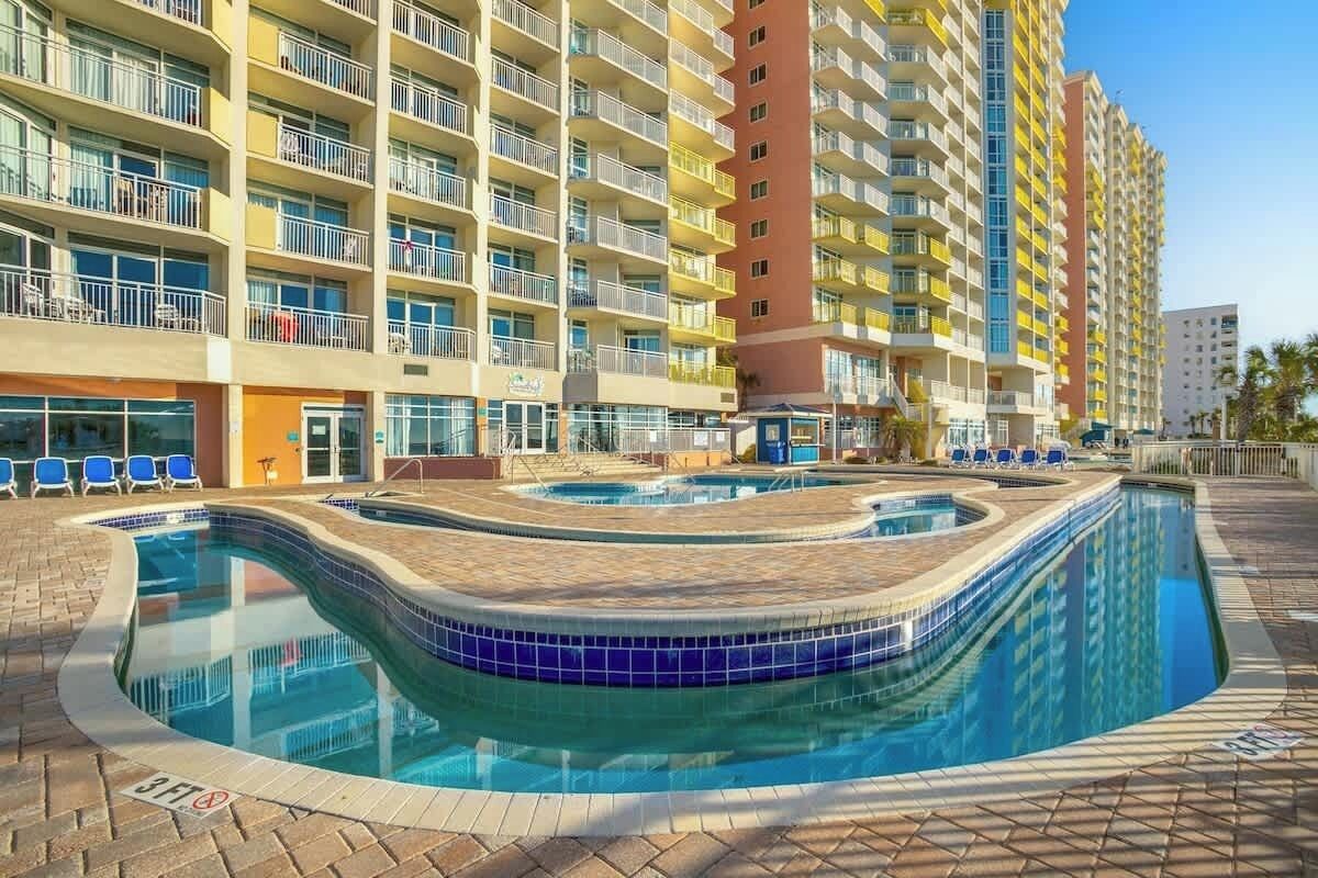 A hotel with a pool area, multiple balconies, and a clear sky.