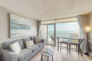 Ein modernes Wohnzimmer mit einer Couch, einem Couchtisch und Blick auf den Ozean durch große Fenster.