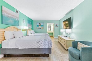 A hotel room with a bed, bedside tables, a dresser, a chair, and artwork on the walls. - Bay Watch Resort 1111 (North Myrtle Beach)