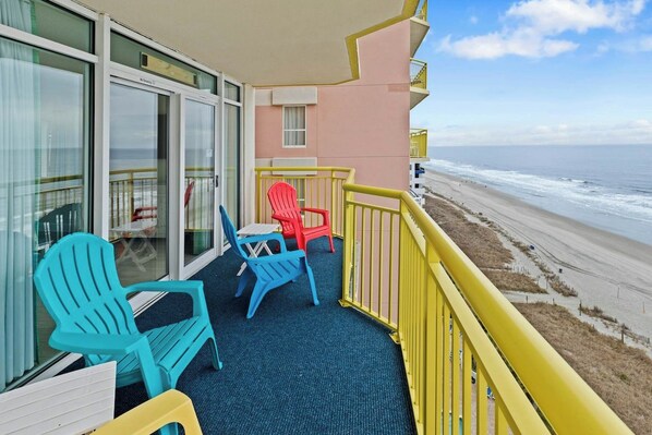A balcony with a view of the beach, featuring a blue carpet, a yellow railing, and colorful chairs. - Bay Watch Resort 1111 (North Myrtle Beach)