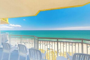 A balcony with white plastic chairs, a view of the beach, and a clear blue sky. - Bay Watch Resort 1022 (North Myrtle Beach)