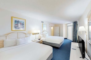 A hotel room with two beds, a desk, a television, and a painting on the wall. - Bay Watch Resort 1022 (North Myrtle Beach)