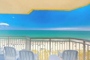 A balcony with white chairs overlooking a beach with umbrellas and people. - Bay Watch Resort 1022 (North Myrtle Beach)