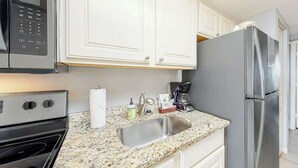 A kitchen with white cabinets, a stainless steel refrigerator, a microwave, a sink, and a stove. - Bay Watch Resort 1238 (North Myrtle Beach)