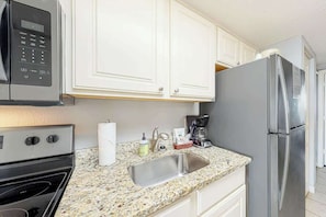 A kitchen with white cabinets, a stainless steel refrigerator, a microwave, a sink, and a stove. - Bay Watch Resort 1238 (North Myrtle Beach)