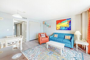 A living room with a sofa, armchair, coffee table, and a painting on the wall. - Bay Watch Resort 1238 (North Myrtle Beach)