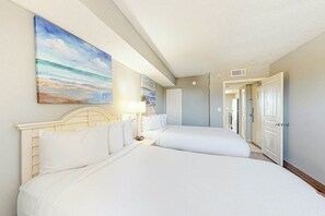 A hotel room with two beds, a painting of a beach scene, and a door leading to a bathroom. - Bay Watch Resort 1238 (North Myrtle Beach)