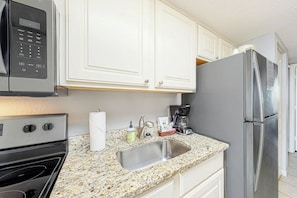 A kitchen with white cabinets, a stainless steel refrigerator, a microwave, and a granite countertop. - Bay Watch Resort 1238 (North Myrtle Beach)