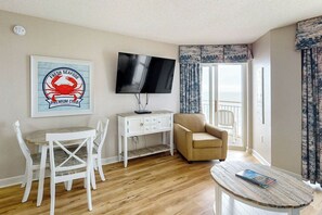 Ein Wohnzimmer mit Fernseher, Esstisch mit Stühlen, einer Couch und einem Fenster mit Vorhängen.