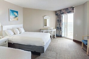 Quarto de hotel com cama, escrivaninha, cadeira e uma grande janela com cortinas.