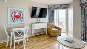 A room with a television, a desk with chairs, a sofa, and a window with curtains. - Bay Watch Resort 1233 (North Myrtle Beach)