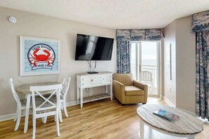 A room with a television, a desk with chairs, a sofa, and a window with curtains. - Bay Watch Resort 1233 (North Myrtle Beach)