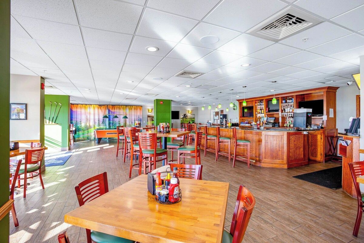 A restaurant with multiple tables and chairs, a bar area, and a view of the outdoors.