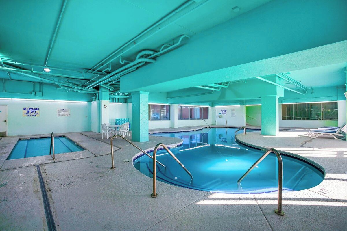 Ein Hallenbad mit mehreren Bahnen, Sicherheitsschildern und Liegestühlen.