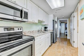 A modern kitchen with white cabinets, a stainless steel microwave, and a built-in oven. - Bay Watch Resort 1038 (North Myrtle Beach)