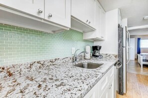 A kitchen with white cabinets, a granite countertop, a stainless steel sink, and a refrigerator. - Bay Watch Resort 1038 (North Myrtle Beach)