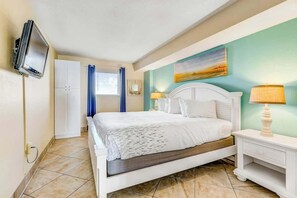 A bedroom with a bed, bedside lamps, a television, and a window with curtains. - Bay Watch Resort 1038 (North Myrtle Beach)