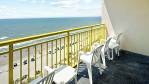 En balkon med udsigt over stranden og havet, med hvide plastikstole og et gult gelænder.