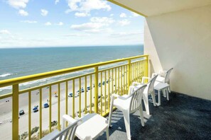 Ein Balkon mit Blick auf Strand und Meer, ausgestattet mit weißen Kunststoffstühlen und einem gelben Geländer.
