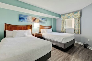A hotel room with two beds, a painting on the wall, a window with curtains, and a bedside table with a lamp. - Bay Watch Resort 1115 (North Myrtle Beach)