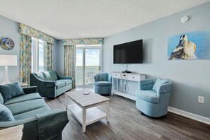 Ein Wohnzimmer mit einer Sofagarnitur, einem Couchtisch, einem an der Wand befestigten Fernseher und einem Gemälde.