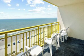 A balcony with a view of the beach and ocean, featuring white plastic chairs and a yellow railing. - Bay Watch Resort 1115 (North Myrtle Beach)