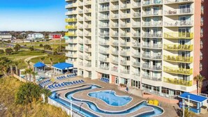 Et hotel med flere etager og et poolområde med en bølgende pool og liggestole.