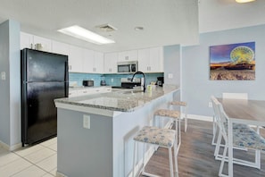 A kitchen with a central island, white cabinets, a black refrigerator, a microwave, and a painting of a Ferris wheel on the wall. - Bay Watch Resort 1115 (North Myrtle Beach)