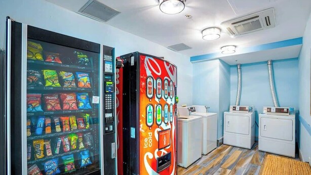 A vending machine with snacks and a Coca-Cola branded machine. There are two washing machines and a sink in the room. - Bay Watch Resort 1121 (North Myrtle Beach)