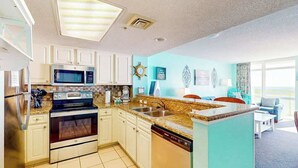 A modern kitchen with built-in appliances, a dining area with a view, and a living room with a large window. - Bay Watch Resort 1121 (North Myrtle Beach)